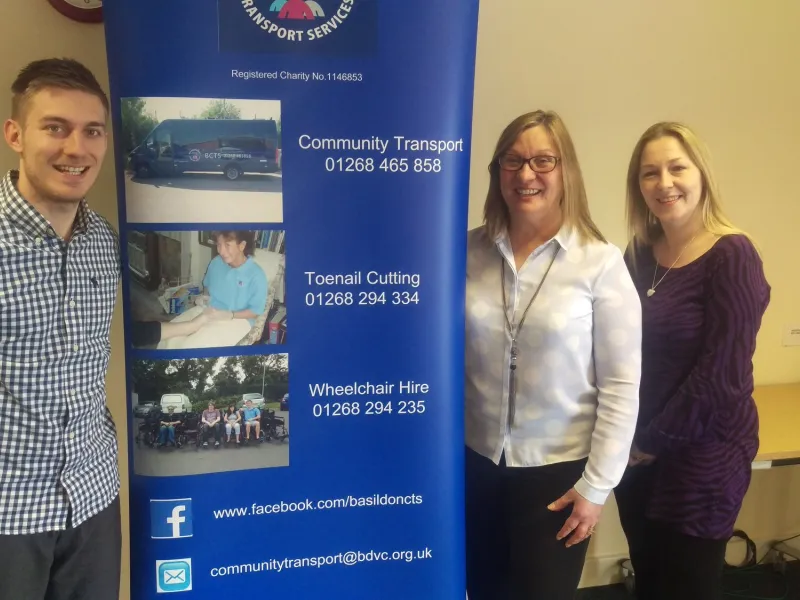 Three members of the office team beside the BCTS banner, which lists the three phone numbers