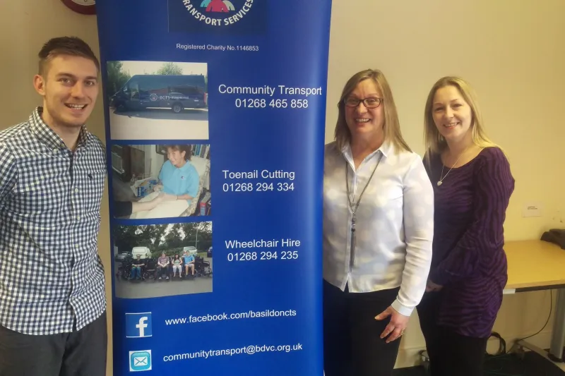 Three members of the office team beside the BCTS banner, which lists the three phone numbers
