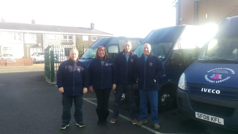 Four BCTS drivers in navy fleeces standing in front of two of our navy minibuses