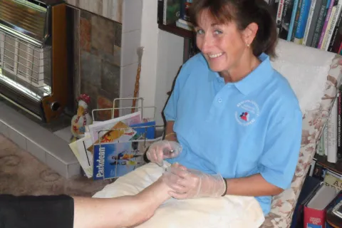 One of our nail cutters, in a BCTS polo shirt and gloves, cutting a client's toenails in their own home